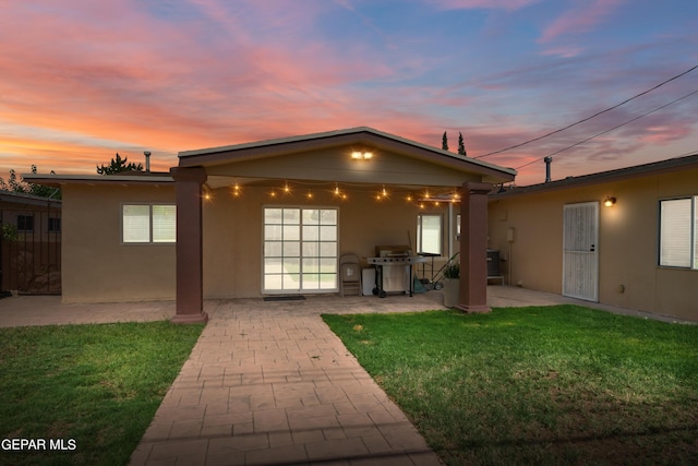 rear view of property with a lawn, a patio area, and stucco siding