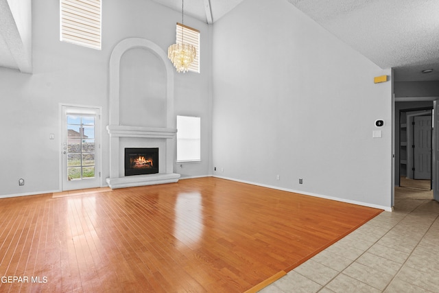 unfurnished living room with plenty of natural light, an inviting chandelier, a large fireplace, and a high ceiling