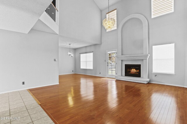 unfurnished living room featuring a fireplace, a high ceiling, a chandelier, and light hardwood / wood-style flooring