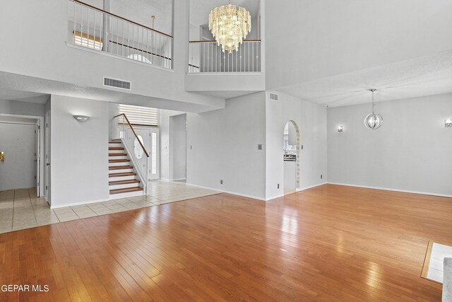 unfurnished living room featuring light hardwood / wood-style floors, a towering ceiling, and a chandelier