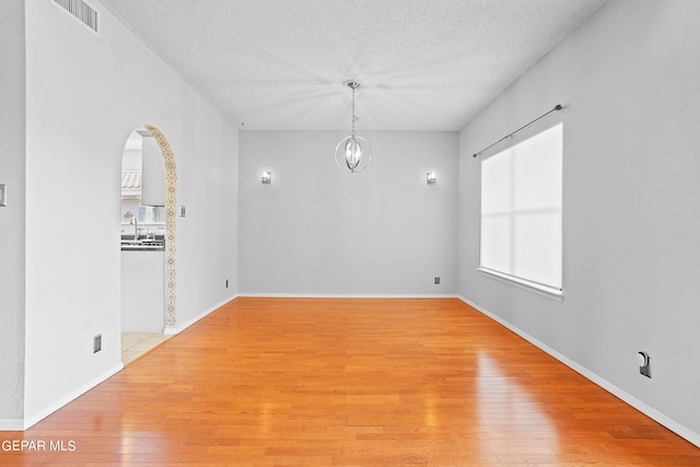 unfurnished room with hardwood / wood-style flooring, sink, a textured ceiling, and an inviting chandelier