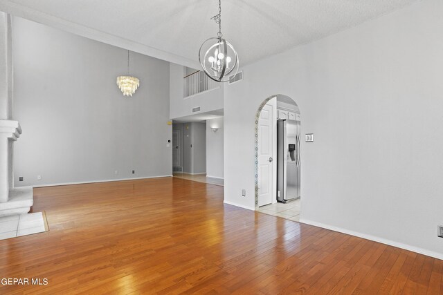 spare room with light wood-type flooring, an inviting chandelier, and a textured ceiling