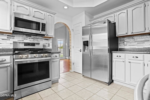 kitchen featuring backsplash, dark stone countertops, light tile patterned floors, appliances with stainless steel finishes, and white cabinets