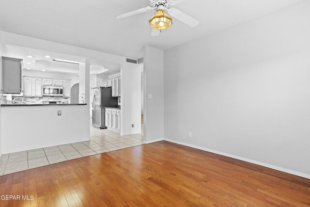 unfurnished living room featuring ceiling fan, light hardwood / wood-style flooring, and sink