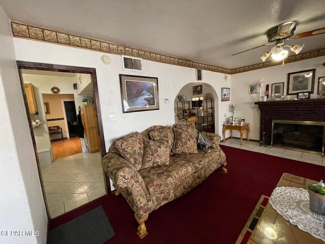 living room with a textured ceiling, ceiling fan, wood-type flooring, and a brick fireplace