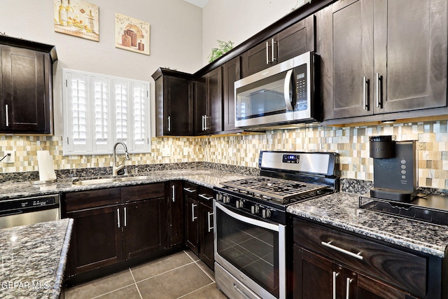 kitchen featuring sink, dark brown cabinets, light tile patterned floors, dark stone countertops, and appliances with stainless steel finishes