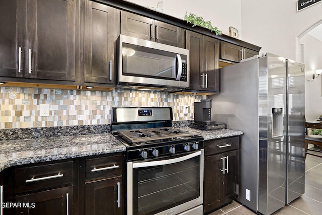 kitchen featuring light tile patterned floors, backsplash, dark brown cabinets, stainless steel appliances, and dark stone counters