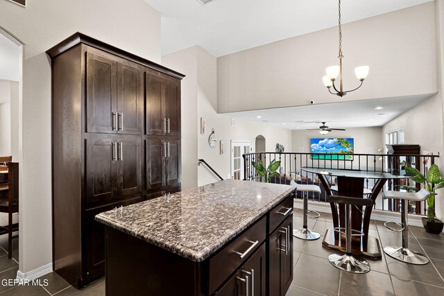 kitchen with pendant lighting, dark stone counters, dark tile patterned floors, a center island, and dark brown cabinets