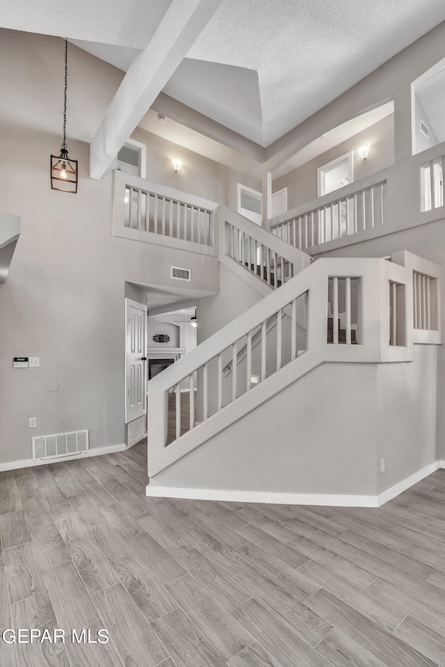 interior space with beamed ceiling, hardwood / wood-style flooring, a high ceiling, and a textured ceiling