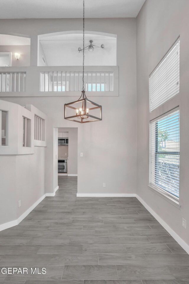 unfurnished living room featuring hardwood / wood-style floors, a towering ceiling, and a chandelier