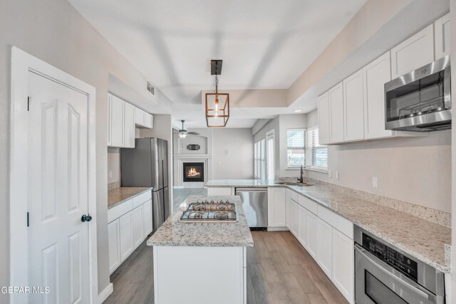 kitchen with hanging light fixtures, hardwood / wood-style flooring, a kitchen island, stainless steel appliances, and white cabinets