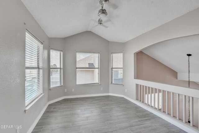 unfurnished room with light hardwood / wood-style floors, vaulted ceiling, a textured ceiling, track lighting, and ceiling fan