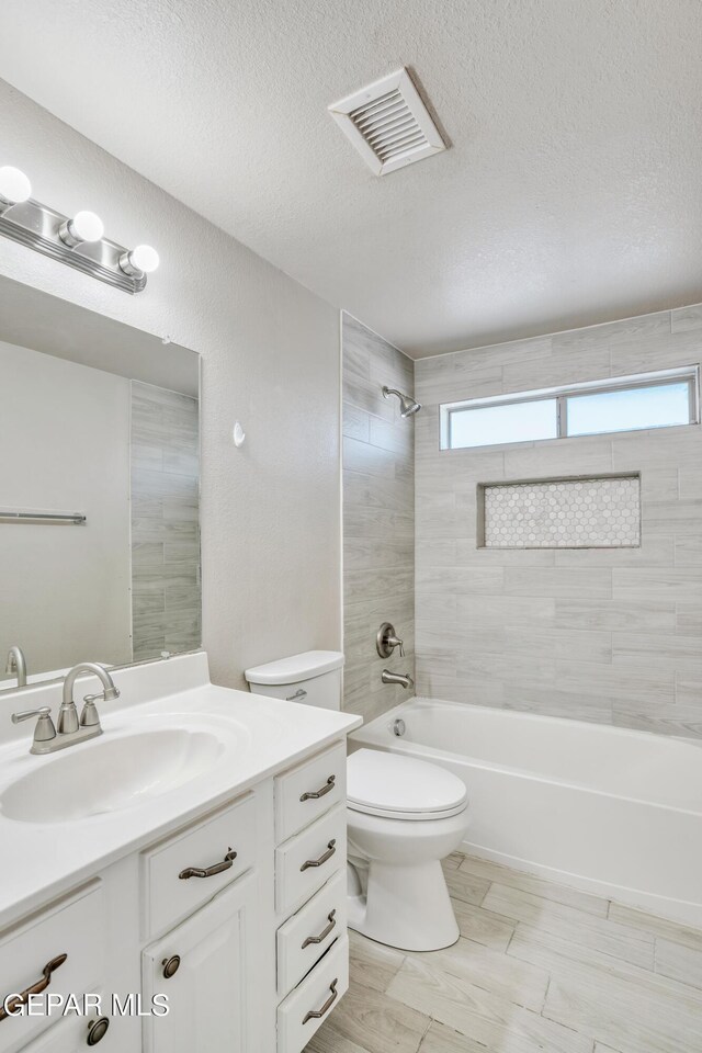 full bathroom featuring tiled shower / bath, a textured ceiling, vanity, and toilet