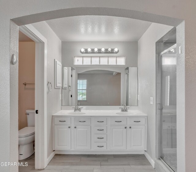 bathroom featuring a textured ceiling, a shower with shower door, dual vanity, and toilet