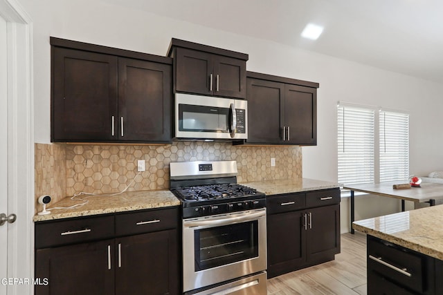 kitchen featuring tasteful backsplash, dark brown cabinetry, light stone counters, light wood-style flooring, and stainless steel appliances