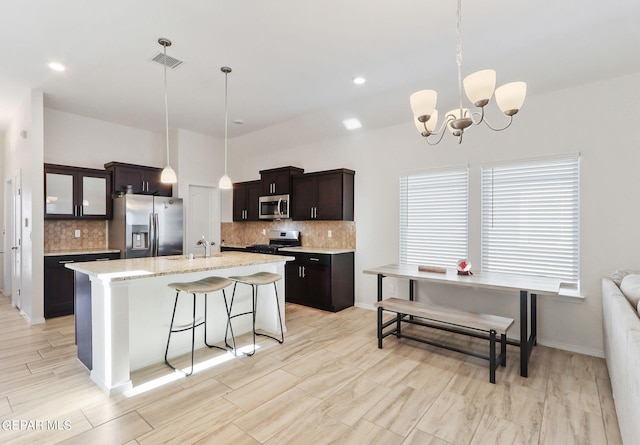 kitchen featuring appliances with stainless steel finishes, tasteful backsplash, pendant lighting, and a kitchen island with sink