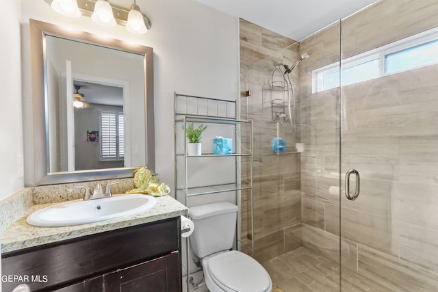 bathroom with a shower with shower door, ceiling fan, toilet, and vanity