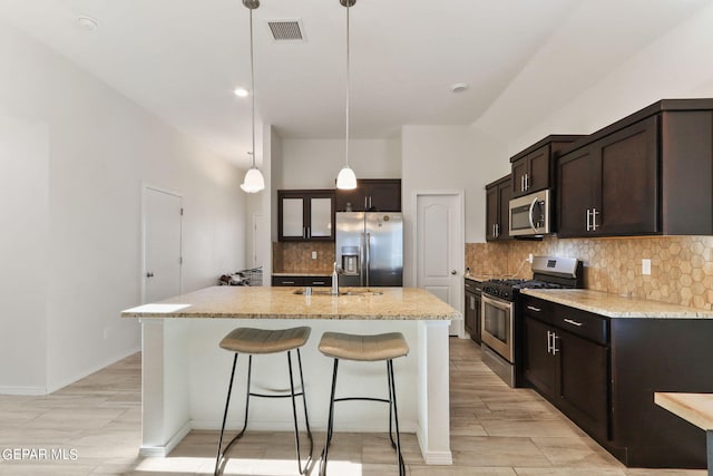 kitchen featuring a center island with sink, stainless steel appliances, light stone counters, and backsplash