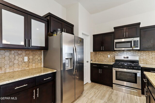 kitchen featuring appliances with stainless steel finishes, light stone counters, decorative backsplash, and dark brown cabinetry