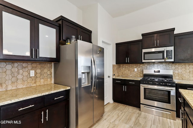 kitchen featuring dark brown cabinets, decorative backsplash, light stone countertops, and appliances with stainless steel finishes