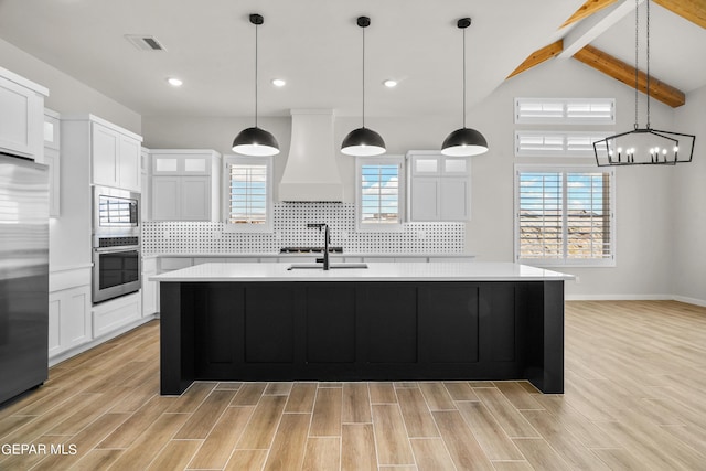 kitchen featuring wood finish floors, custom exhaust hood, light countertops, visible vents, and built in appliances