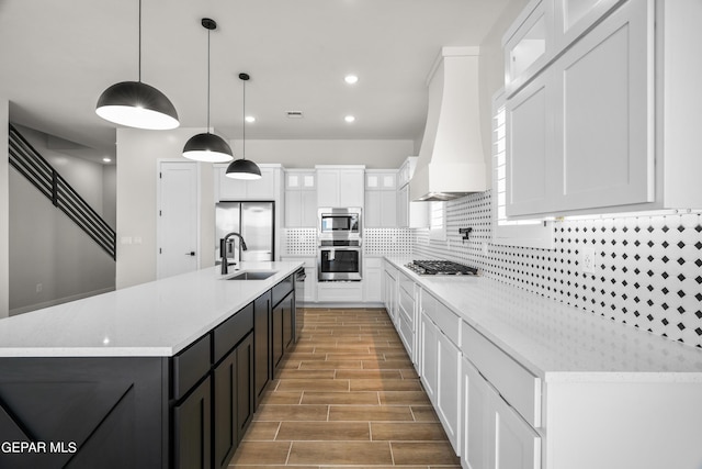 kitchen with custom range hood, decorative backsplash, appliances with stainless steel finishes, white cabinets, and a sink