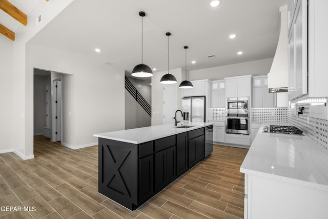 kitchen with wood finish floors, backsplash, appliances with stainless steel finishes, white cabinets, and a sink