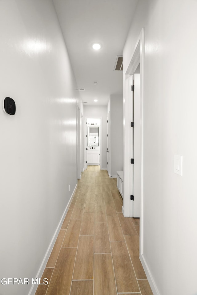 hallway with wood finish floors, visible vents, baseboards, and recessed lighting