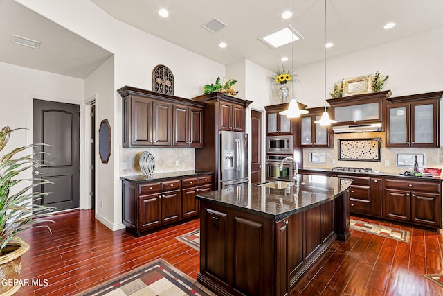 kitchen with an island with sink, decorative light fixtures, backsplash, dark wood-type flooring, and appliances with stainless steel finishes