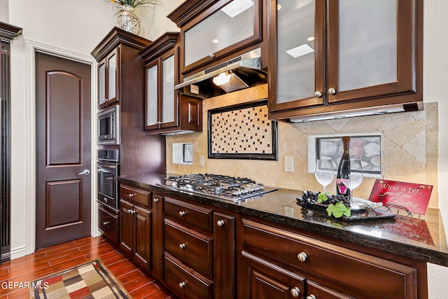 kitchen with appliances with stainless steel finishes, dark stone countertops, backsplash, ventilation hood, and dark hardwood / wood-style floors