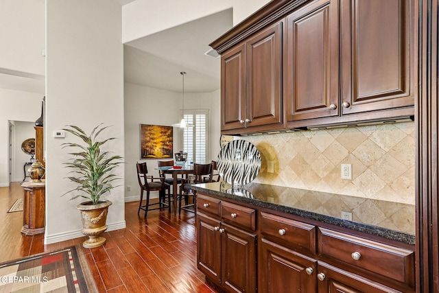 kitchen featuring backsplash, hanging light fixtures, dark stone counters, and dark hardwood / wood-style floors