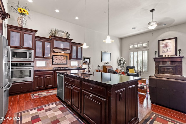 kitchen featuring an island with sink, sink, tasteful backsplash, dark wood-type flooring, and appliances with stainless steel finishes