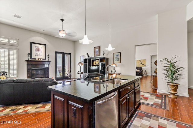 kitchen featuring dark brown cabinetry, an island with sink, hanging light fixtures, stainless steel dishwasher, and hardwood / wood-style floors