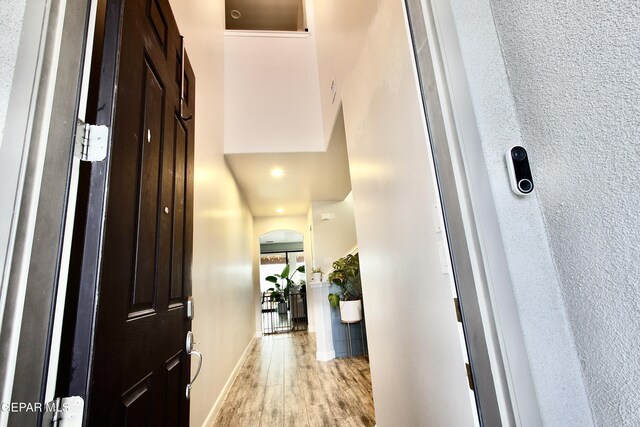 hallway with baseboards, a high ceiling, and light wood-style flooring
