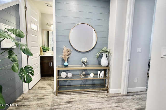 interior space with baseboards, visible vents, wood finished floors, and wood walls