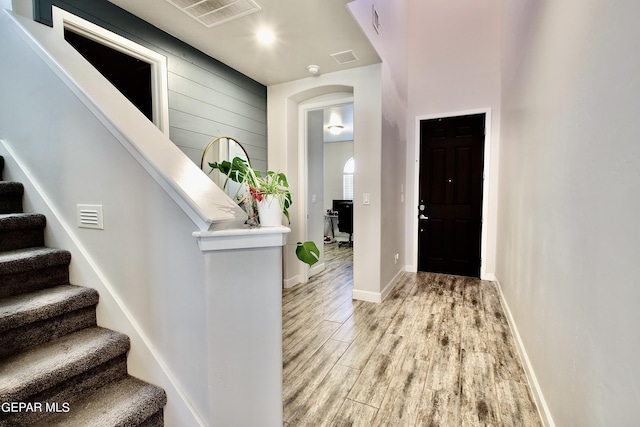 foyer entrance with light wood-style flooring, arched walkways, stairway, and visible vents