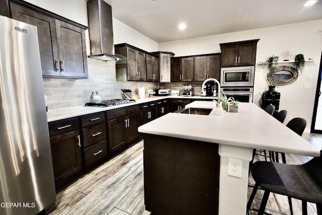 kitchen featuring a sink, wall chimney exhaust hood, tasteful backsplash, a kitchen breakfast bar, and stainless steel appliances