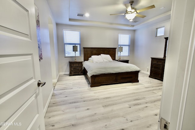 bedroom featuring baseboards, a tray ceiling, visible vents, and light wood-style floors