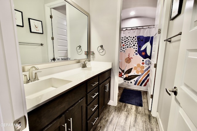 full bath with double vanity, a sink, toilet, and wood finished floors