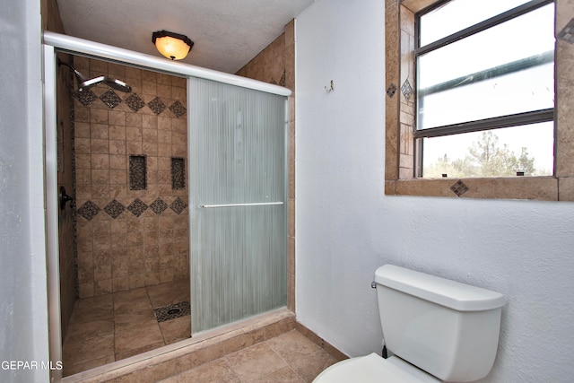 bathroom with a textured ceiling, a shower with door, tile patterned flooring, and toilet