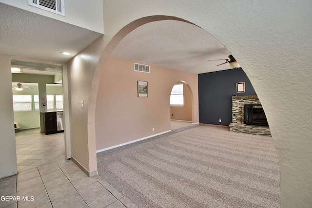 unfurnished living room with ceiling fan, a fireplace, a textured ceiling, and light carpet