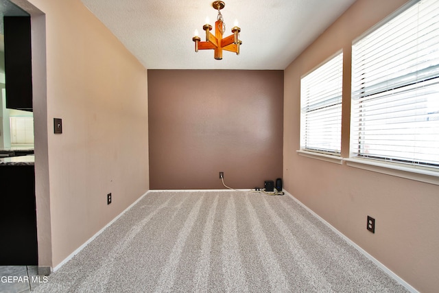 carpeted spare room featuring a textured ceiling and a chandelier