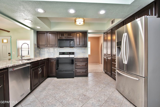 kitchen with stainless steel appliances, decorative backsplash, light stone countertops, sink, and a tray ceiling