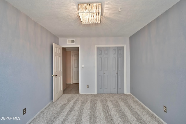 unfurnished bedroom featuring an inviting chandelier, a closet, a textured ceiling, and carpet floors