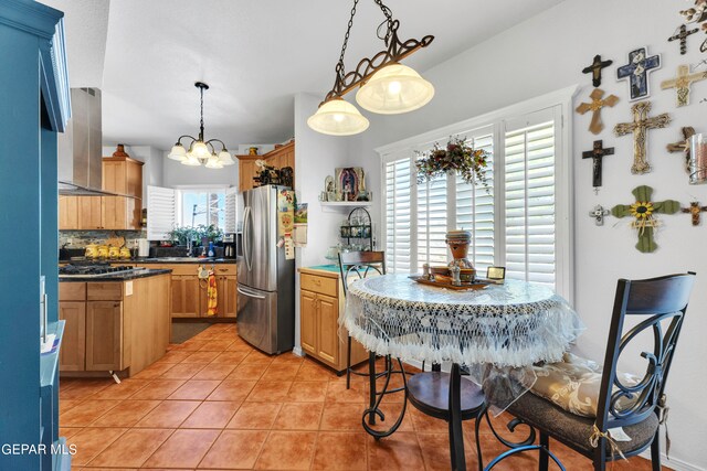 kitchen featuring appliances with stainless steel finishes, backsplash, wall chimney exhaust hood, a wealth of natural light, and light tile patterned floors