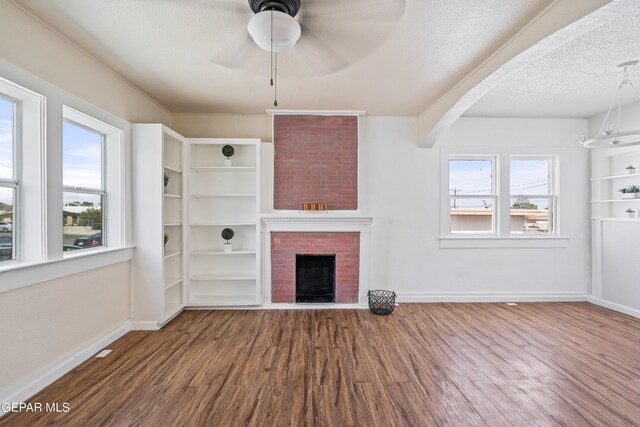 unfurnished living room featuring a textured ceiling, a brick fireplace, built in features, hardwood / wood-style flooring, and ceiling fan