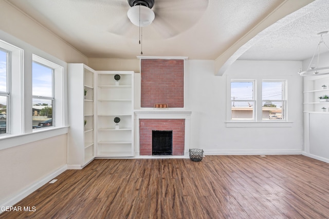 unfurnished living room featuring dark wood-type flooring, a fireplace, a textured ceiling, and a wealth of natural light