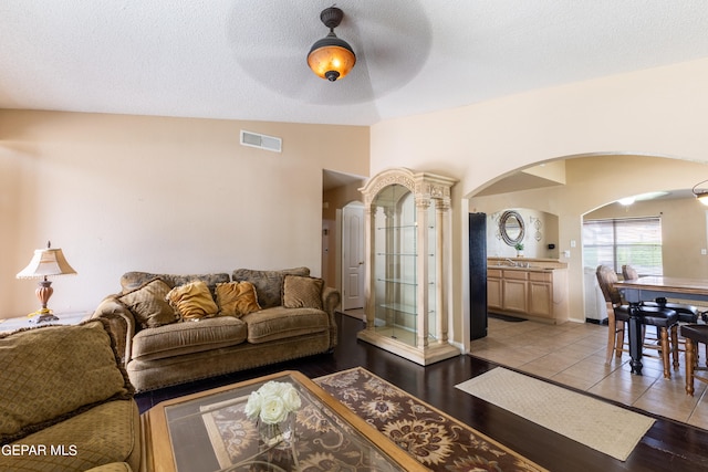 living room with ceiling fan, light tile patterned flooring, a textured ceiling, and vaulted ceiling