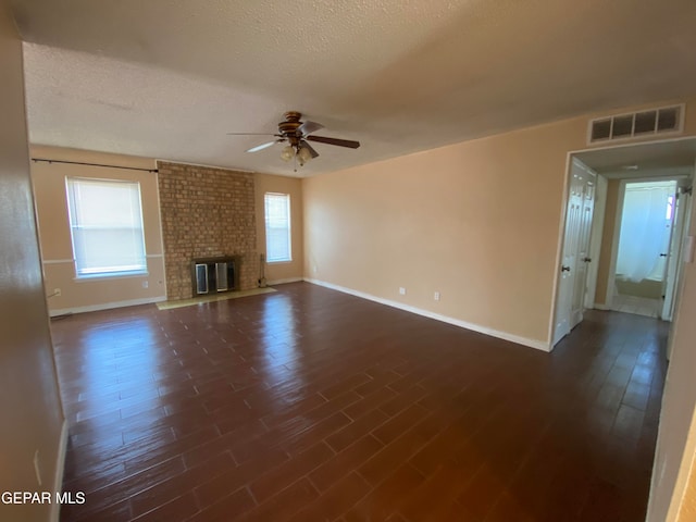 unfurnished living room featuring a brick fireplace, a textured ceiling, dark hardwood / wood-style floors, and ceiling fan