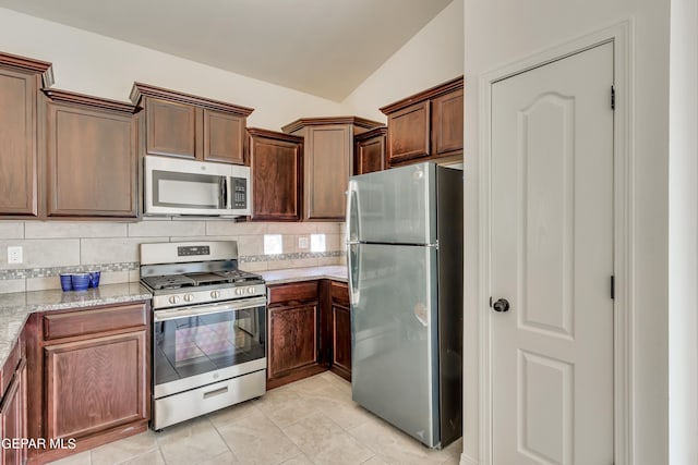 kitchen featuring light tile patterned floors, decorative backsplash, appliances with stainless steel finishes, vaulted ceiling, and light stone counters